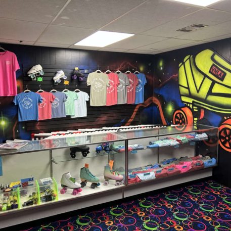 A vibrant skate shop interior featuring colorful t-shirts, roller skates, and a neon-patterned floor, highlighted by a skate mural.