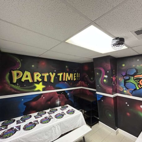 Vibrant party room featuring "PARTY TIME!!" graffiti, colorful murals, and a table set with themed plates, ideal for celebrations.
