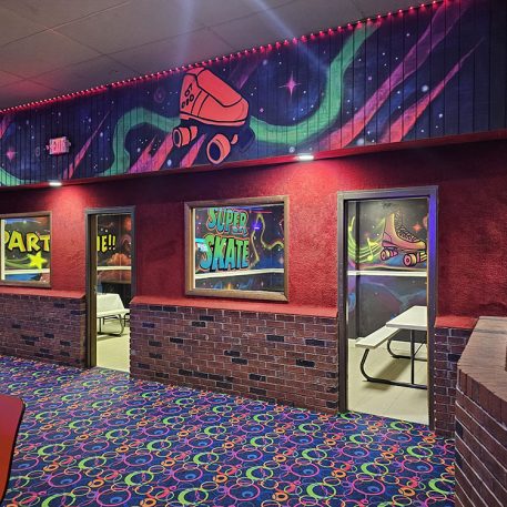 Entrance to a vibrant roller skating rink featuring colorful murals, window signs for 'Art' and 'Super Skate', and bright carpet.