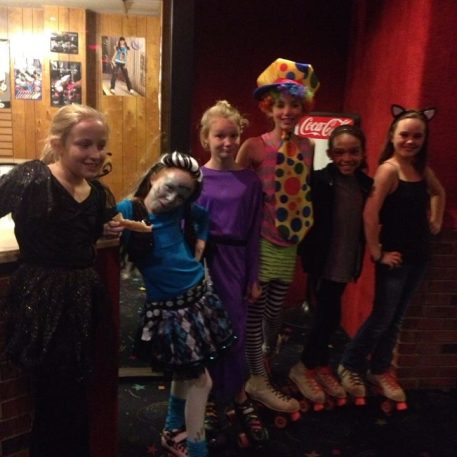 A group of children in colorful costumes and roller skates poses together in a brightly decorated roller rink.