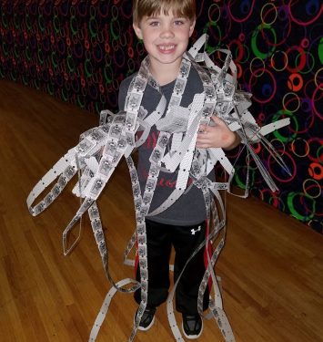 A young boy proudly holds up a colorful bunch of papers, smiling at the camera.