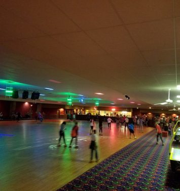 A busy bowling alley with players at the lanes and others walking around, enjoying the lively atmosphere.