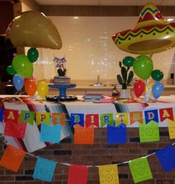 A festive birthday party scene featuring colorful balloons, a Mexican flag, and a traditional sombrero.