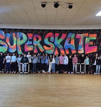 A diverse group of people smiling and posing in front of a vibrant, large mural.