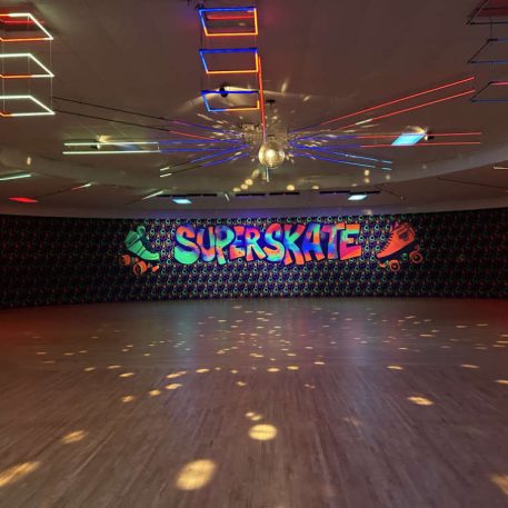 A vibrant roller skating rink featuring colorful lights and the bold "SUPERSKATE" mural against a patterned wall.