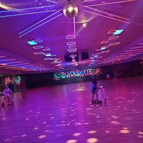 A vibrant roller skating rink with colorful lights, a disco ball, and a mural reading "SUPERSKATE," lively atmosphere with skaters.