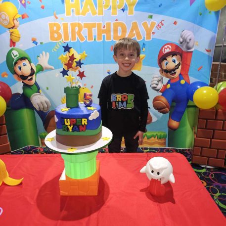 A colorful birthday celebration featuring a cake with "SUPER RYAN," decorations of popular game characters, and vibrant balloons.