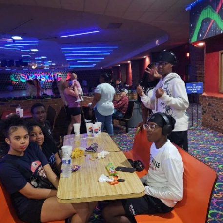 A vibrant roller skating rink scene with colorful decor, featuring skaters and people socializing at tables.