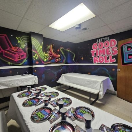 Colorful party room with vibrant graffiti, including skateboards and a record player, featuring tables set for celebration.