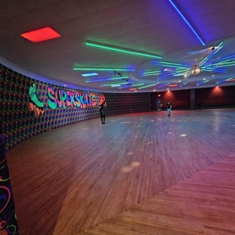 Colorful roller skating rink named "Superskate," featuring vibrant neon lights, disco ball, and two skaters on a wooden floor.