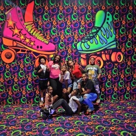 A group of people poses playfully in front of a vibrant, neon roller skate mural with colorful swirl patterns.