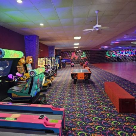A colorful roller skating rink with arcade games and vibrant carpet; "Superskate" sign visible in the background.