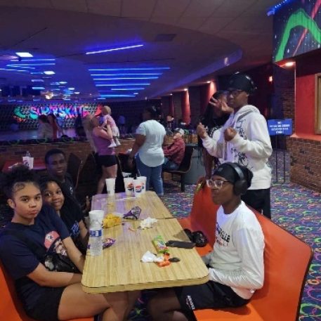A group of young people enjoys snacks at a roller skating rink, surrounded by colorful lights and a vibrant atmosphere.