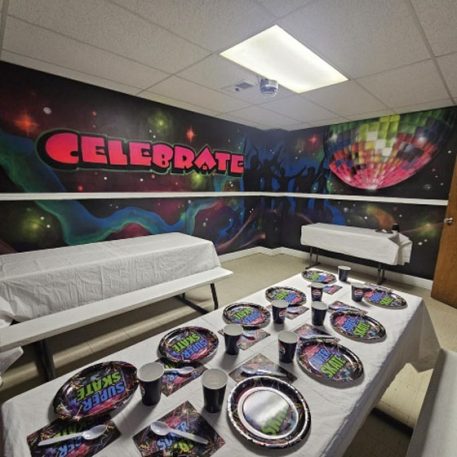 A vibrant party room with "Celebrate" mural, decorated tables, and colorful plates and cups for a festive atmosphere.