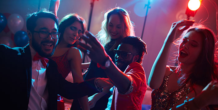 A lively group of people dance and enjoy a festive atmosphere with colorful lighting and confetti in the background.