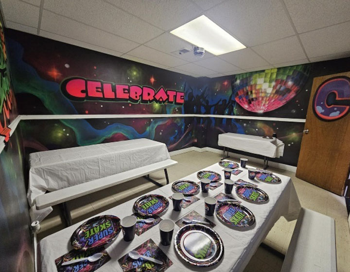 A vibrant party room with "Celebrate" mural, decorated tables, and colorful plates and cups for a festive atmosphere.