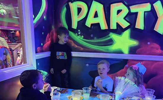 A colorful party scene featuring children sitting at a table with snacks and cups, surrounded by vibrant wall art.