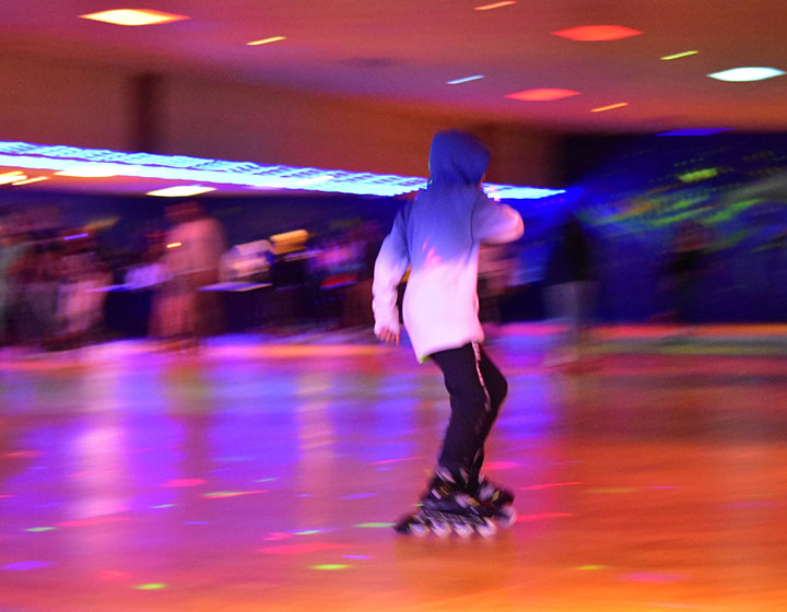 A child in a hoodie glides on roller skates, surrounded by colorful lights in a vibrant skating rink. Motion blur adds excitement.